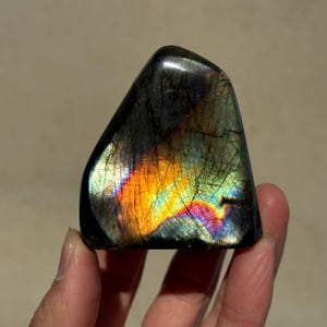 May include: A large, iridescent labradorite crystal with a black base and a rainbow of colors, including orange, yellow, green, blue, and purple.