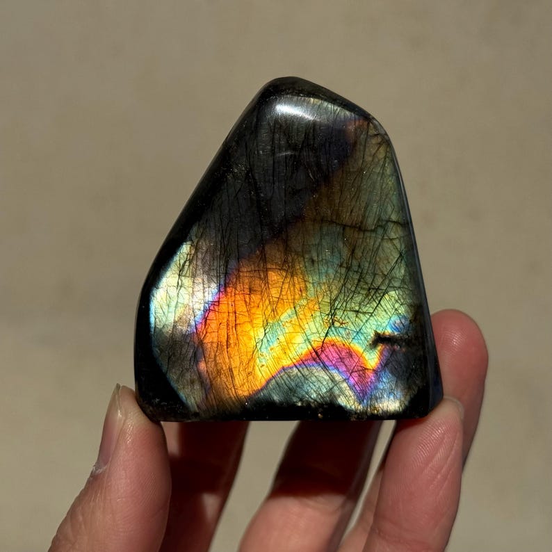 May include: A large, iridescent labradorite crystal with a black base and a rainbow of colors, including orange, yellow, green, blue, and purple.