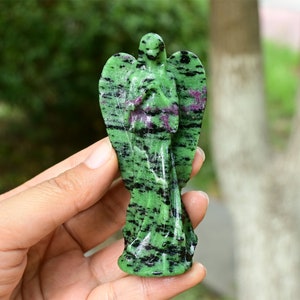 May include: Green and black gemstone angel figurine carved from a single piece of stone. The angel is standing with its wings spread out and its hands clasped in prayer.