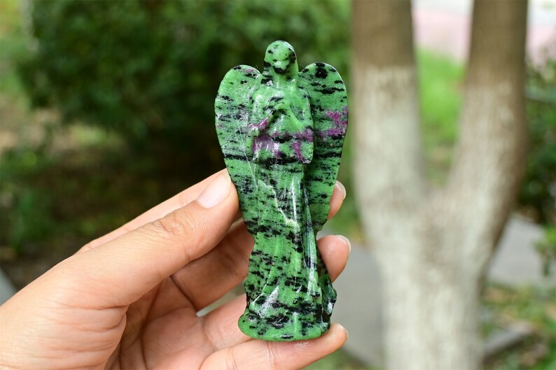 May include: Green and black gemstone angel figurine carved from a single piece of stone. The angel is standing with its wings spread out and its hands clasped in prayer.