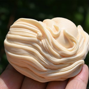 May include: A small, ivory-colored sculpture of a woman's head with long, flowing hair. The sculpture is carved in a detailed and realistic style.