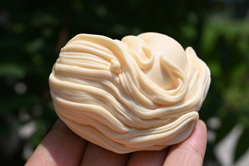May include: A small, ivory-colored sculpture of a woman's head with long, flowing hair. The sculpture is carved in a detailed and realistic style.