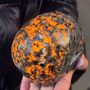 May include: A black and orange skull-shaped object with a speckled pattern. The object is made of a smooth, hard material.
