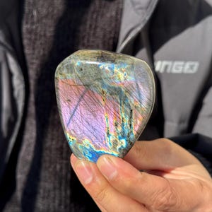 May include: A polished, iridescent labradorite stone with a heart shape. The stone displays a rainbow of colors, including purple, blue, green, and gold.
