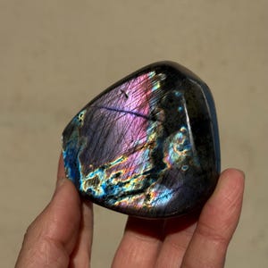 May include: A large, iridescent labradorite crystal with a deep purple hue and flashes of blue, green, and gold. The crystal is smooth and polished, with a natural, irregular shape.