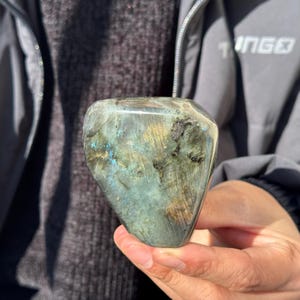 May include: A large, freeform, polished labradorite crystal with a green, blue, and gold iridescent sheen.