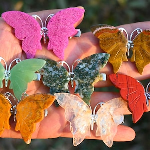 May include: Seven butterfly-shaped hair clips made of different types of stone. The clips are in various colours, including green, pink, orange, red, brown, and white.