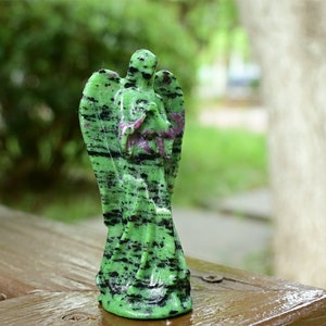 May include: Green and black gemstone angel figurine. The angel is carved from a green stone with black streaks and has its wings outstretched.