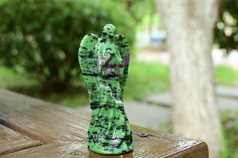 May include: Green and black gemstone angel figurine. The angel is carved from a green stone with black streaks and has its wings outstretched.