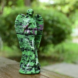 May include: Green and black gemstone angel figurine with wings. The angel is carved in a standing pose with its hands clasped in prayer.
