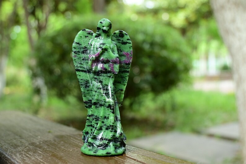May include: Green and black gemstone angel figurine with wings. The angel is carved in a standing pose with its hands clasped in prayer.