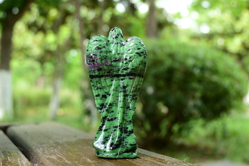 May include: Green and black gemstone angel figurine with wings. The angel is carved from a green stone with black and pink streaks.