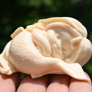 May include: A small, white, carved figurine of a sleeping mermaid with a detailed tail and long hair.