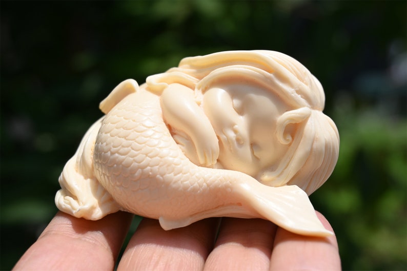 May include: A small, white, carved figurine of a sleeping mermaid with a detailed tail and long hair.
