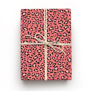 May include: A rectangular gift box wrapped in coral-colored paper with a leopard print pattern in black and pink. The box is tied with a natural twine bow, creating a visually appealing presentation. The overall theme is gift-giving.
