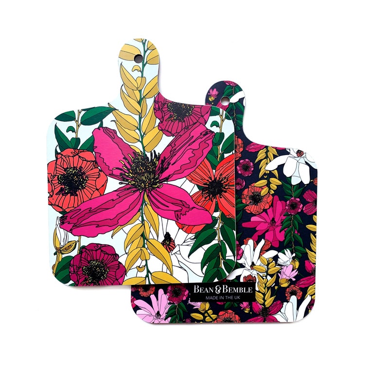 May include: Two floral patterned cutting boards with a white background and a black background. The white board has pink, red, and yellow flowers. The black board has pink, red, and white flowers. The text "Bean & Bemble Made in the UK" is on the black board.