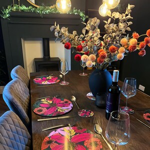 May include: A dining table setting with floral placemats, wine glasses, and a bottle of wine. The table is set with silverware and a vase of flowers in the center.