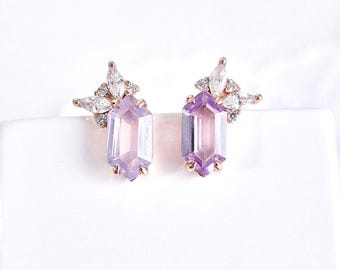 May include: A pair of stud earrings featuring a light purple, rectangular gemstone with a cluster of white, teardrop-shaped stones above. The earrings have a rose gold setting and are displayed on a white surface.