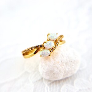 May include: A gold ring with three oval-shaped white opals and small clear stones set in a twisted band.