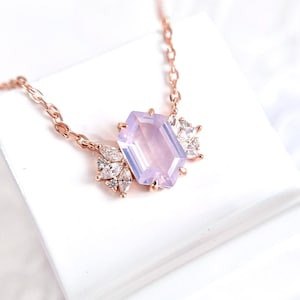 May include: Rose gold necklace featuring a large, light purple rectangular gemstone as the focal point. The pendant is accented with smaller, clear gemstones in a leaf-like arrangement. The chain is delicate and complements the pendant's design.