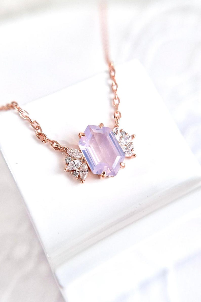 May include: Rose gold necklace featuring a large, light purple rectangular gemstone as the focal point. The pendant is accented with smaller, clear gemstones in a leaf-like arrangement. The chain is delicate and complements the pendant's design.