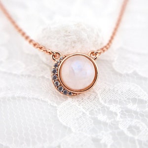May include: A delicate rose gold necklace with a round moonstone pendant surrounded by a crescent moon of sparkling clear stones.