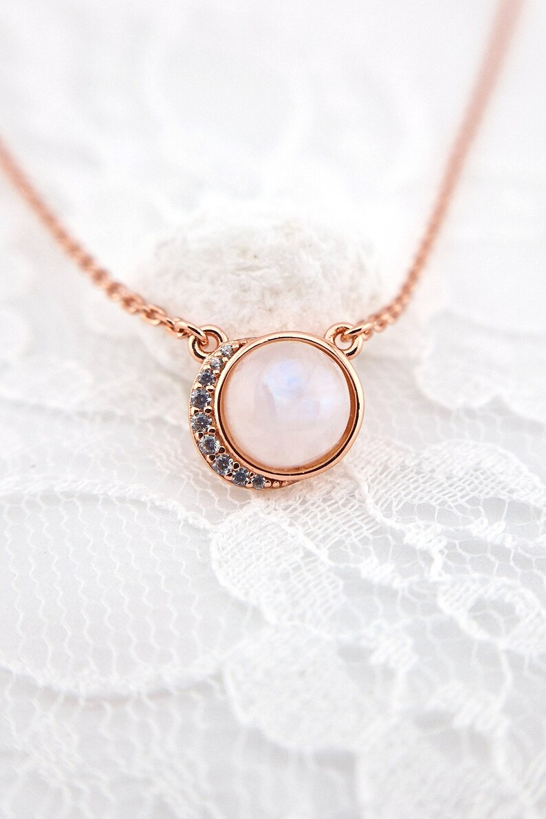 May include: A delicate rose gold necklace with a round moonstone pendant surrounded by a crescent moon of sparkling clear stones.