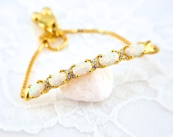 May include: A gold bracelet with a row of white opal stones set in a gold chain. The bracelet has a sliding clasp for adjustable sizing.