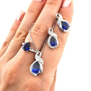 May include: A silver necklace, ring, and earrings set with a blue pear-shaped gemstone surrounded by smaller clear gemstones.