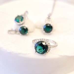 May include: A silver ring with a large, round, dark green gemstone surrounded by a halo of smaller, clear gemstones.