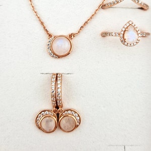 May include: A set of rose gold jewelry featuring moonstone and cubic zirconia. The set includes a necklace, a ring, and a pair of earrings.