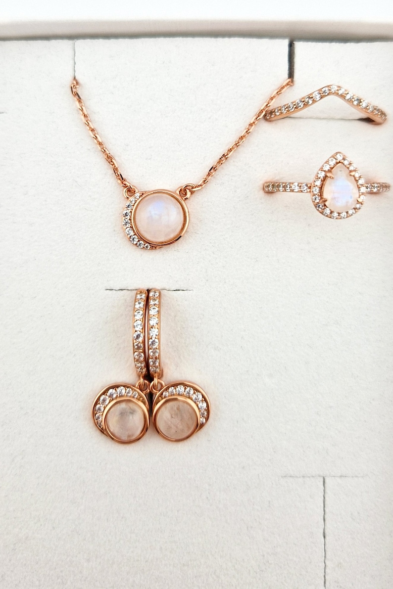 May include: A set of rose gold jewelry featuring moonstone and cubic zirconia. The set includes a necklace, a ring, and a pair of earrings.