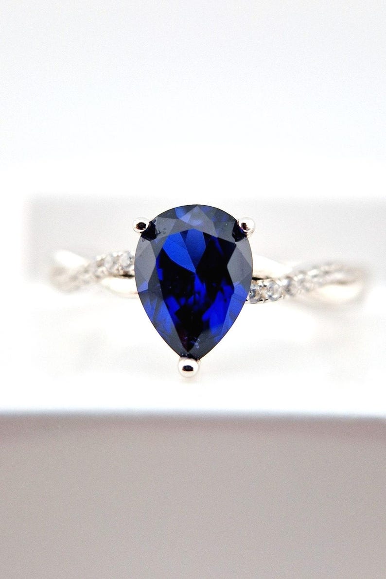 May include: A silver ring with a pear-shaped blue sapphire gemstone and smaller clear gemstones on the band.