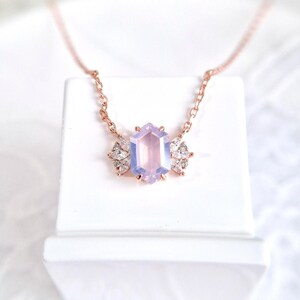 Peut inclure: Un collier en or rose orn&eacute; d'un pendentif en forme d'hexagone de couleur lavande. Le pendentif est flanqu&eacute; de deux groupes de petits pierres pr&eacute;cieuses transparentes. Le collier est pr&eacute;sent&eacute; sur une surface blanche.