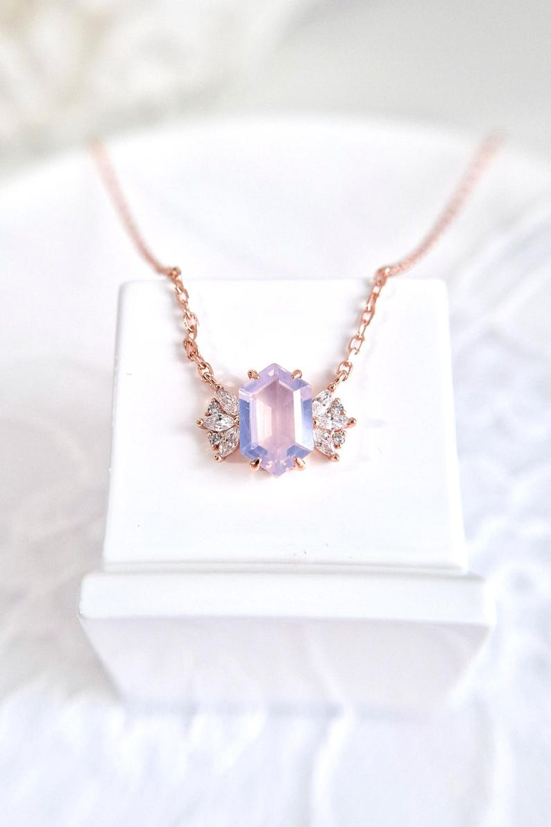 Peut inclure: Un collier en or rose orn&eacute; d'un pendentif en forme d'hexagone de couleur lavande. Le pendentif est flanqu&eacute; de deux groupes de petits pierres pr&eacute;cieuses transparentes. Le collier est pr&eacute;sent&eacute; sur une surface blanche.