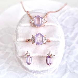 Peut inclure: Un ensemble de bijoux comprenant un collier, une bague et des boucles d'oreilles. L'ensemble comprend un collier en or rose avec un pendentif en pierre pr&eacute;cieuse hexagonale de couleur lavande. La bague et les boucles d'oreilles pr&eacute;sentent &eacute;galement le m&ecirc;me design de pierre pr&eacute;cieuse.