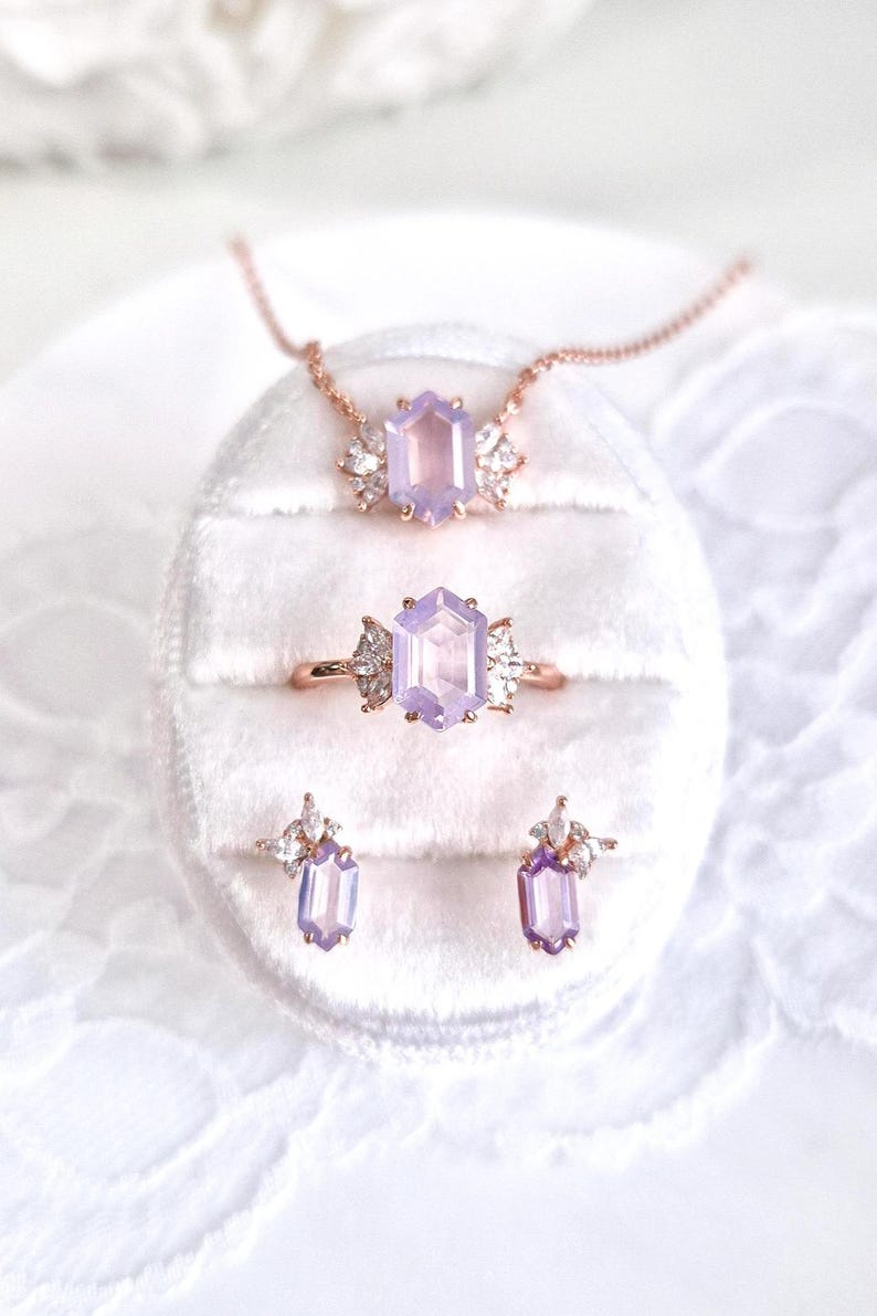Peut inclure: Un ensemble de bijoux comprenant un collier, une bague et des boucles d'oreilles. L'ensemble comprend un collier en or rose avec un pendentif en pierre pr&eacute;cieuse hexagonale de couleur lavande. La bague et les boucles d'oreilles pr&eacute;sentent &eacute;galement le m&ecirc;me design de pierre pr&eacute;cieuse.