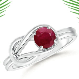 May include: A silver ring with a red ruby gemstone set in a knot design.