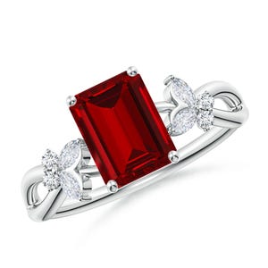 May include: A silver ring with a large, red, emerald-cut gemstone. The ring features two butterfly-shaped accents with smaller, clear gemstones.