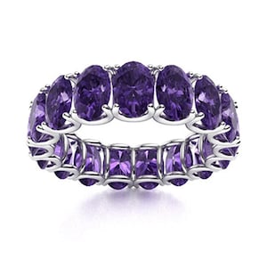 May include: A silver ring featuring a continuous band of oval-cut, deep purple gemstones. The ring's design includes a row of rectangular purple stones at the base, creating a striking contrast. The gemstones are set in a silver band.