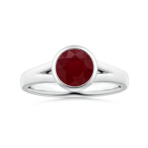 Peut inclure: Une bague en argent ornée d'une grosse pierre rouge foncé et ronde. La pierre est sertie dans un sertissage à lunette, et la monture est fendue. La bague est présentée sur fond blanc.