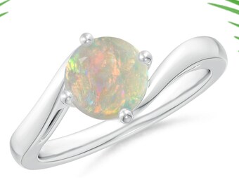 Puede incluir: Un anillo de plata con una piedra preciosa de ópalo blanco engastada en garras. La banda del anillo es curva y tiene un acabado pulido.