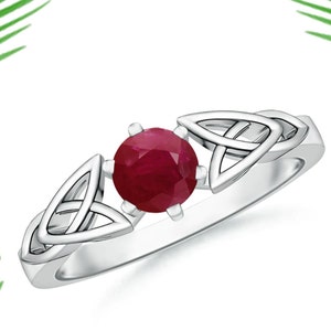 以下が含まれることがあります： ケルトの結び目のデザインに赤いルビーの宝石がセットされたシルバーリング