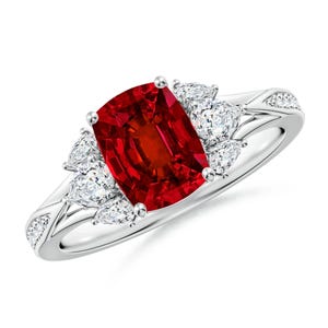 Può includere: Un anello in oro bianco con una pietra preziosa rossa a forma di cuscino e tre pietre di accento a forma di pera. L'anello ha un design delicato e intricato.