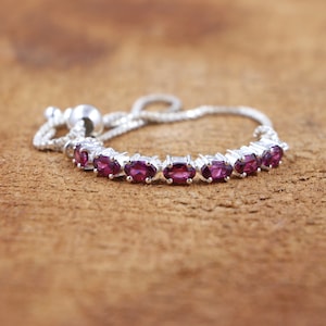 Peut inclure: Un bracelet en argent avec un fermoir coulissant et une rangée de pierres précieuses ovales de couleur violette.