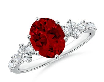 May include: A silver ring featuring a large oval red gemstone, surrounded by smaller white gemstones in a floral design.