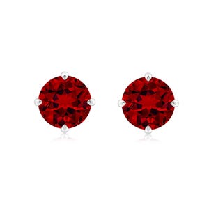 Peut inclure: Une paire de boucles d'oreilles à clous rondes avec des pierres précieuses facettées rouge foncé serties dans des griffes en métal argenté. Chaque pierre circulaire présente une taille brillant avec de multiples facettes réfléchissant la lumière.