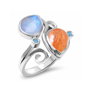 Puede incluir: Un anillo de plata con una piedra de luna azul y una piedra de sol naranja. El anillo tiene un diseño delicado y en espiral y dos pequeñas piedras azules.