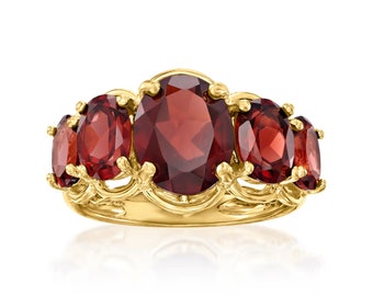 May include: A gold-toned ring featuring five oval-cut, deep red gemstones. The gemstones are set in a decorative, ornate setting. The ring's design is symmetrical, with the largest gemstone in the center.