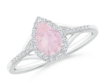 May include: A silver ring featuring a pear-shaped, light pink gemstone surrounded by a halo of smaller, clear gemstones. The ring's band splits into two delicate, gem-studded strands on either side of the main stone.